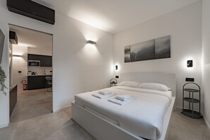 A modern bedroom with a bed, bedside tables, a wall-mounted artwork, and a kitchen area visible through an open door. - 9 min. Walk from Porta Nuova, Design and Elegance (Milan)