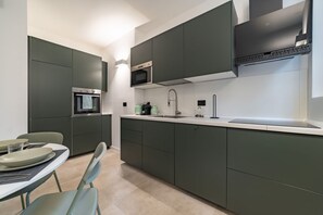 A modern kitchen with dark cabinets, a microwave, a sink, and a dining area with chairs and plates. - 9 min. Walk from Porta Nuova, Design and Elegance (Milan)