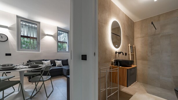 Un interior moderno con zona de comedor, sofá y un baño con espejo grande y lavamanos.
