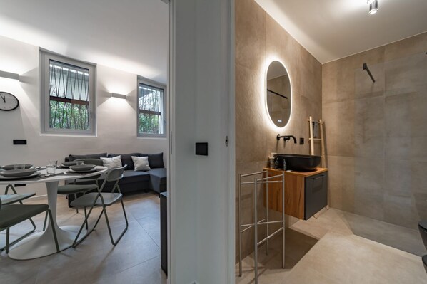 A modern interior with a dining area, sofa, and a bathroom with a large mirror and sink. - 9 min. Walk from Porta Nuova, Design and Elegance (Milan)