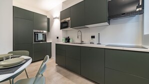 Cocina moderna con armarios oscuros, un microondas, un fregadero y un comedor con sillas y platos.