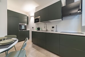A modern kitchen with dark cabinets, a microwave, a sink, and a dining area with chairs and plates. - 9 min. Walk from Porta Nuova, Design and Elegance (Milan)