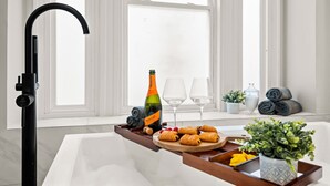 Une salle de bain moderne avec une baignoire, un plateau en bois avec des en-cas, une bouteille de champagne et une plante en pot.
