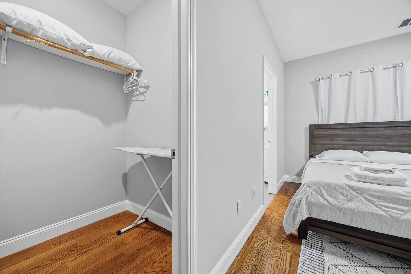 A bedroom with a bed, a wooden floor, a white wall, and a door.