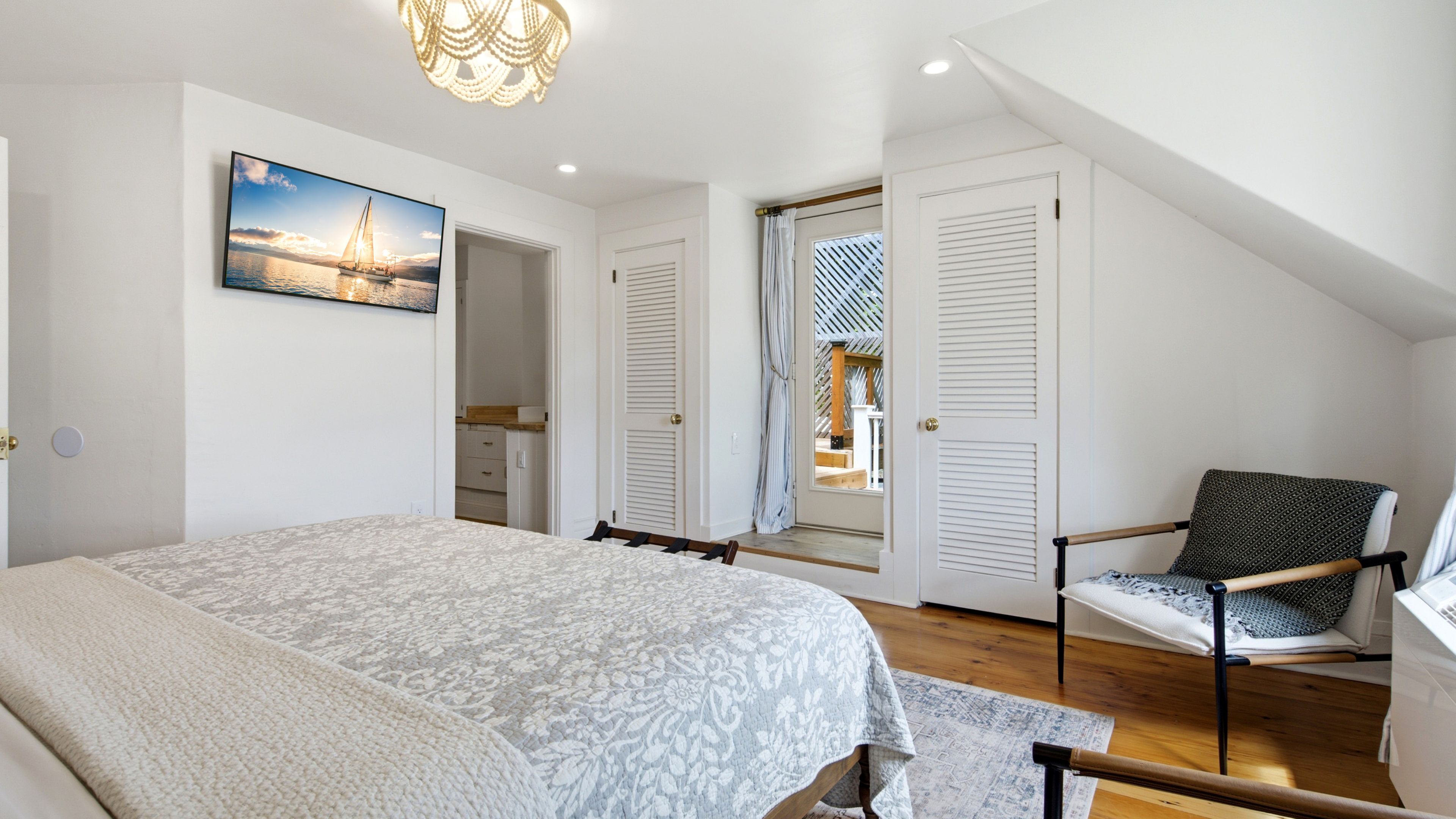 A bedroom with a bed, a chair, a painting, and a view through a door.