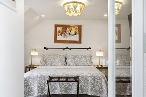 Une chambre à coucher avec un lit, des lampes de chevet, un lustre, un tableau encadré au mur et un miroir.
