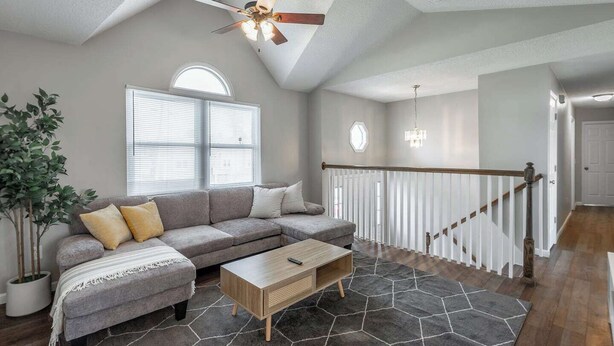 A modern living room with a sectional sofa, a wooden coffee table, a ceiling fan, and a staircase with a railing.