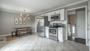 A modern kitchen with a stainless steel refrigerator, microwave, and oven, a dining area with a bench, and a hallway with a door.