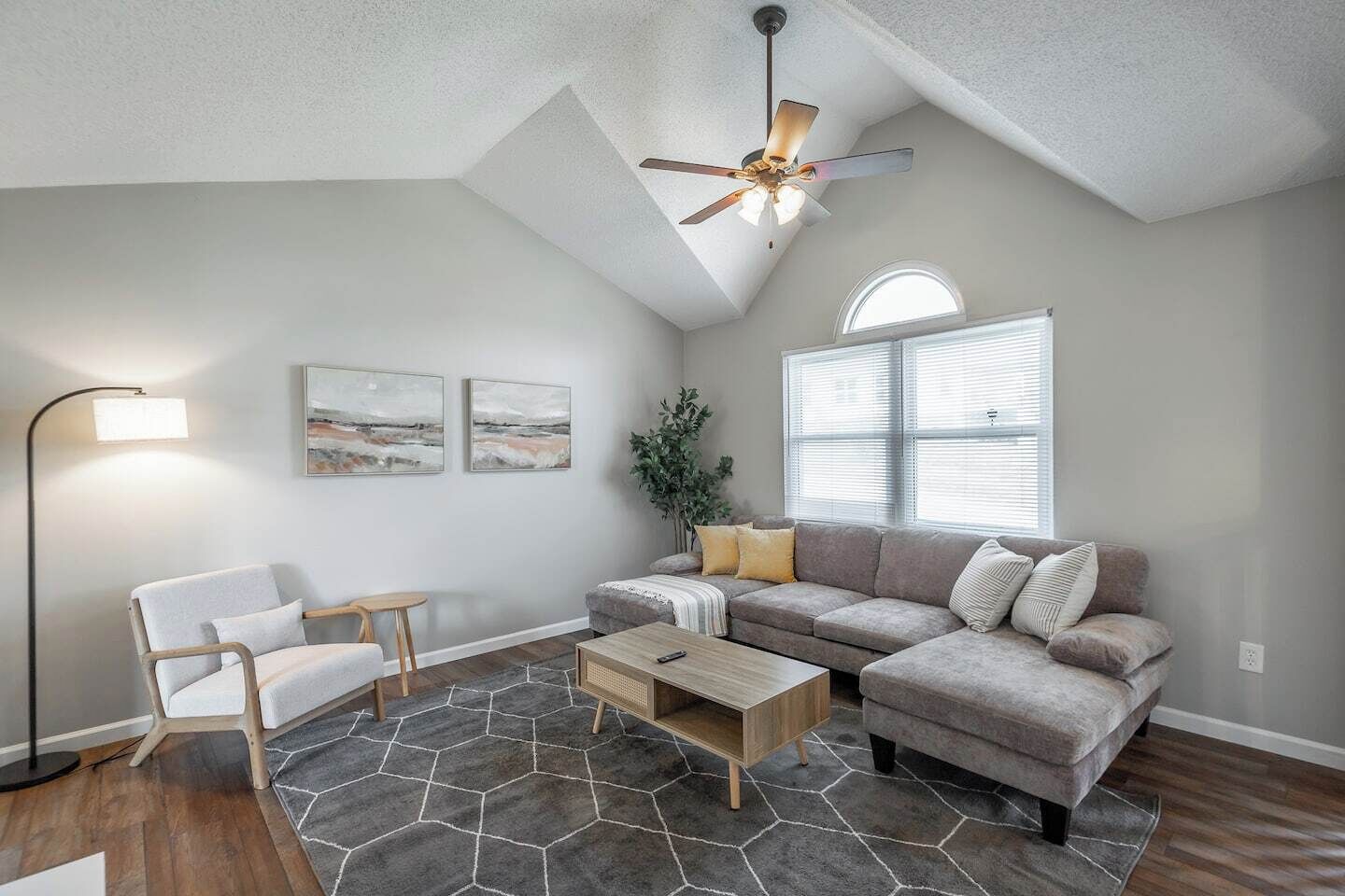 A living room with a gray sofa, a wooden coffee table, a floor lamp, and a ceiling fan.