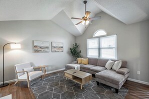 Ein Wohnzimmer mit grauem Sofa, einem Holztisch, einer Stehlampe und einem Deckenventilator.