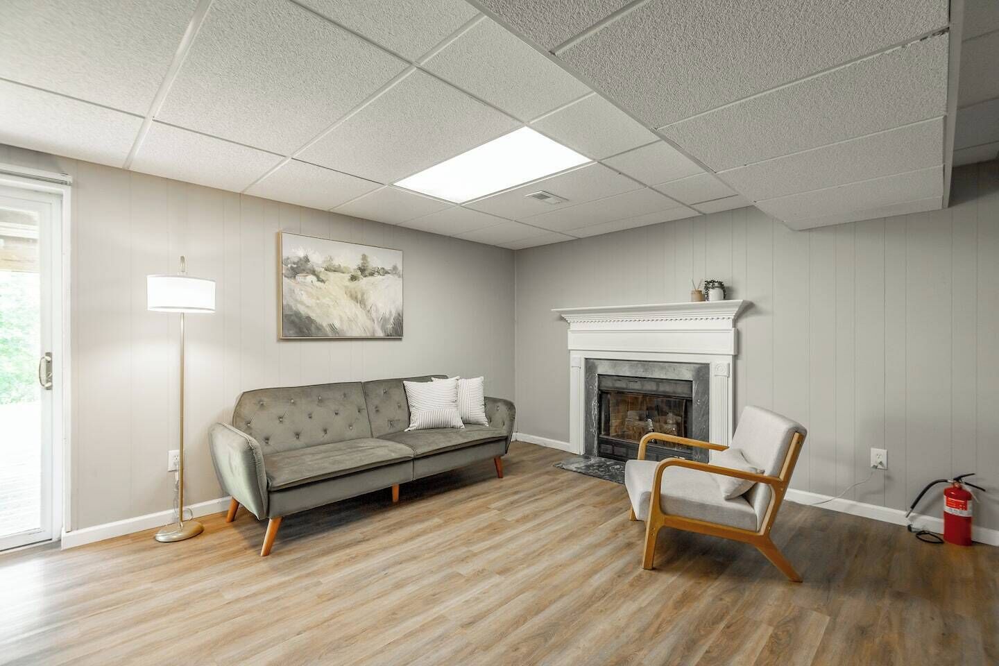 Ein Wohnzimmer mit grauem Sofa, einem Holzstuhl, einem Kamin und einem Bild an der Wand.