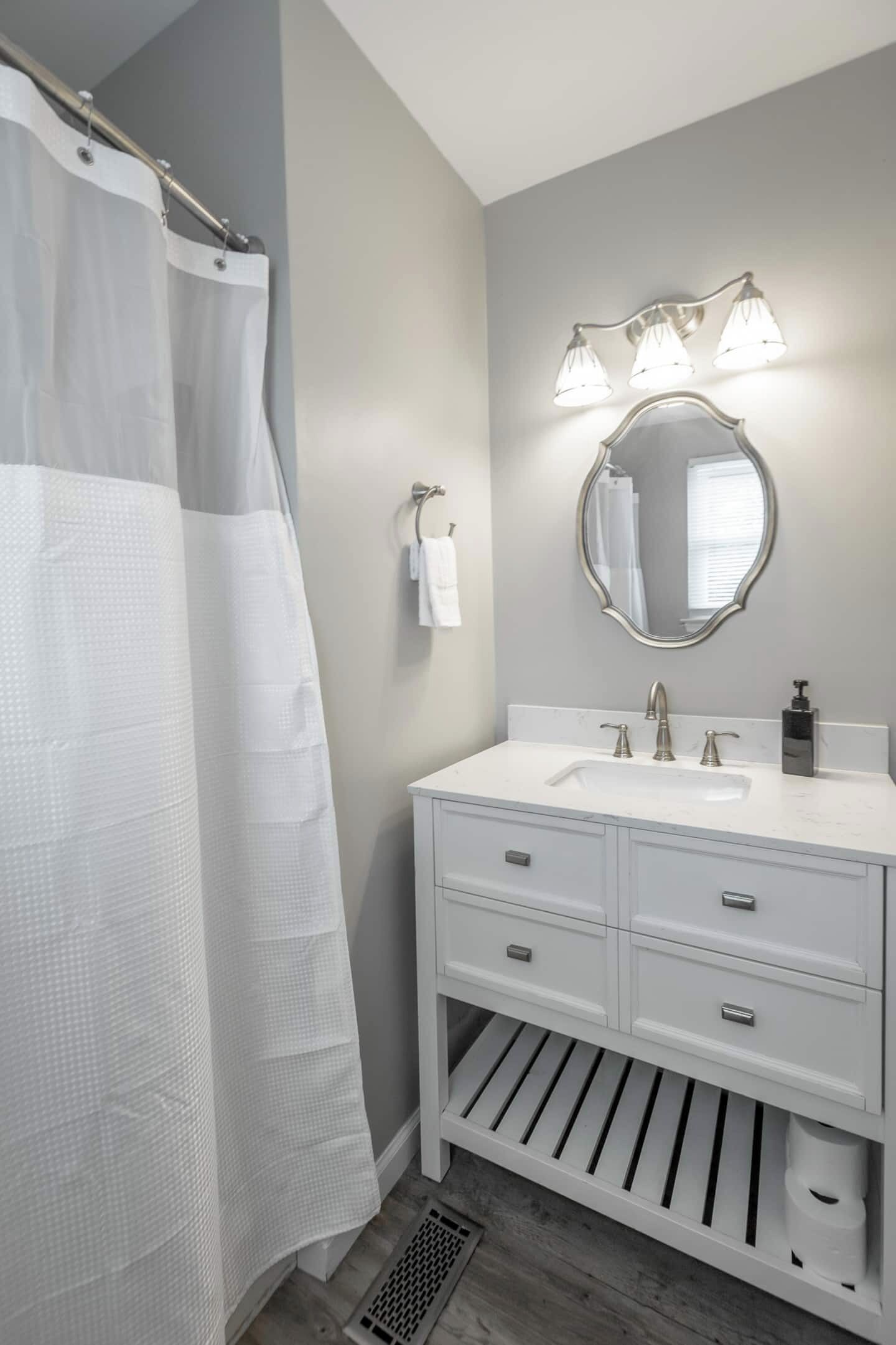 Un baño con cortina de ducha, un lavabo con espejo y una lámpara sobre el espejo.