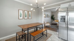 A modern kitchen with a wooden dining table, benches, a stainless steel refrigerator, and framed artwork on the wall.