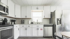 Een moderne keuken met witte kasten, roestvrijstalen apparatuur en een raam boven de spoelbak.
