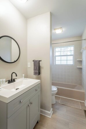 Une salle de bain moderne avec un meuble-lavabo blanc, un miroir rond, des toilettes et une baignoire.