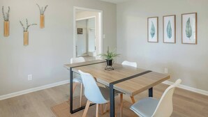 Un comedor con una mesa de madera, sillas blancas y una planta en maceta.