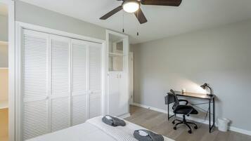 Une chambre à coucher comprenant un lit, un bureau avec une chaise, un ventilateur de plafond et une armoire avec des portes coulissantes.