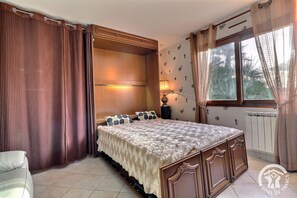 Ein Schlafzimmer mit einem großen Bett, einem Holz-Kopfstück, einem Nachttisch, einer Lampe und einem Fenster mit Vorhängen.