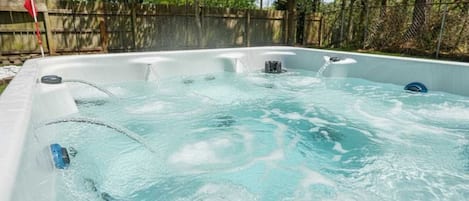 A hot tub with water jets, surrounded by a wooden fence and trees.