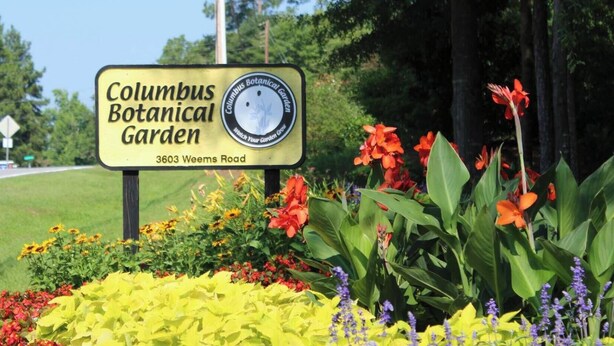 A sign for Columbus Botanical Garden with a variety of colorful flowers in the foreground.
