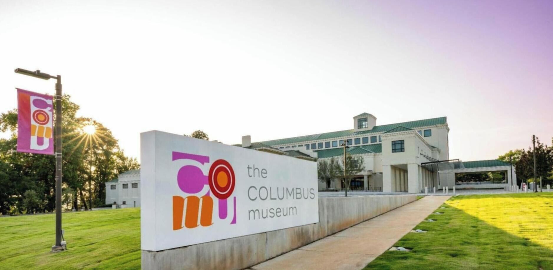 A sign for the Columbus Museum with a modern building in the background.