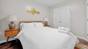 A neatly made bed with white linens, two bedside tables with lamps, a wall art piece, and a door.