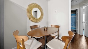 A dining area with a round table, four wooden chairs, and a gold-framed mirror on the wall.