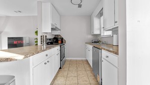A modern kitchen with white cabinets, granite countertops, and a tiled floor.