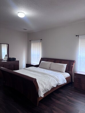 Een slaapkamer met een houten bed, nachtkastje, dressoir en een plafondlamp.