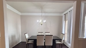 A dining room with a dark wood table and four chairs, a chandelier, and large windows with blinds. - 5bd Beautiful Modern house in Spring/The Woodlands (Spring)