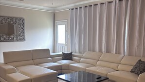 A living room with a sectional sofa, a glass coffee table, a ceiling fan, and a large window with curtains. - 5bd Beautiful Modern house in Spring/The Woodlands (Spring)