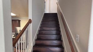A staircase with dark wooden steps and white railings, leading to a room with a visible kitchen area. - 5bd Beautiful Modern house in Spring/The Woodlands (Spring)