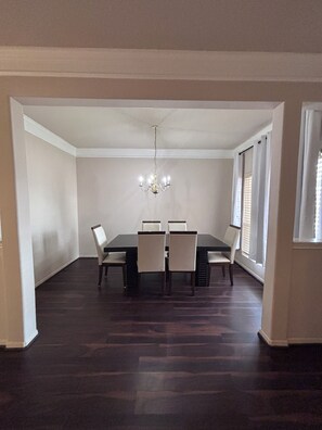 Een eetzaal met een donker houten vloer, een kroonluchter en een tafel met vier stoelen.