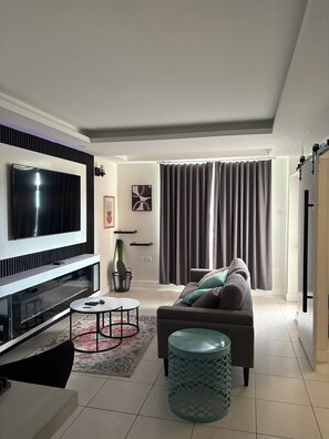 Ein modernes Wohnzimmer mit Flachbildfernseher, einer Couch, einem Couchtisch und einem gemusterten Teppich.