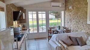 A compact kitchen with a refrigerator, microwave, and sink. A dining area with a table and chairs is visible through a glass door. A white sofa with cushions is in the foreground. - Rent in Mas Provençal in the heart of the Luberon, apartment 2 Rooms (Pertuis)