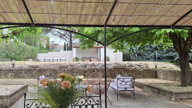 An outdoor seating area with tables and chairs, surrounded by trees and a stone wall. - Rent in Mas Provençal in the heart of the Luberon, apartment 2 Rooms (Pertuis)