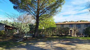 A stone building with a tiled roof, surrounded by trees and a gravel path. - Rent in Mas Provençal in the heart of the Luberon, apartment 2 Rooms (Pertuis)