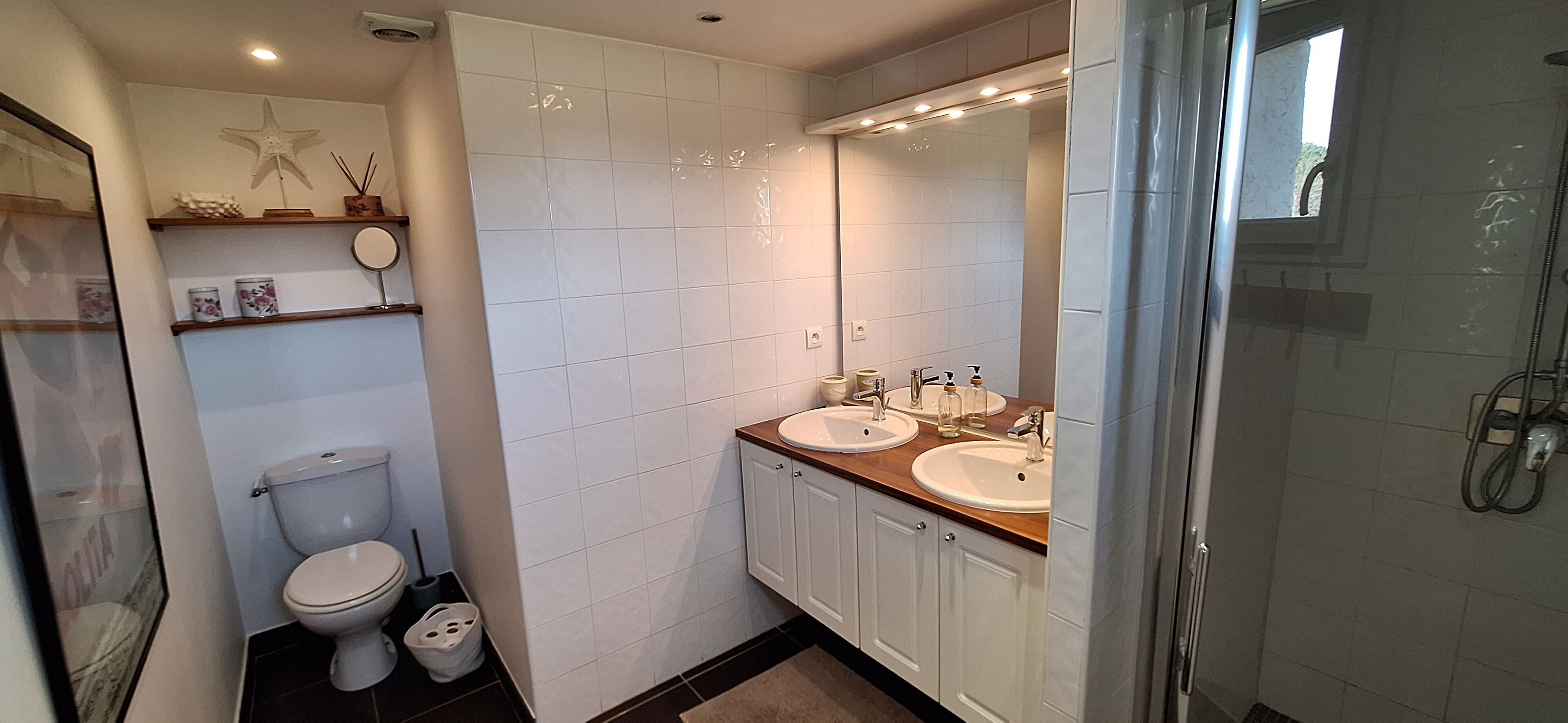 Un baño con inodoro, dos lavamanos, ducha y un espejo grande.