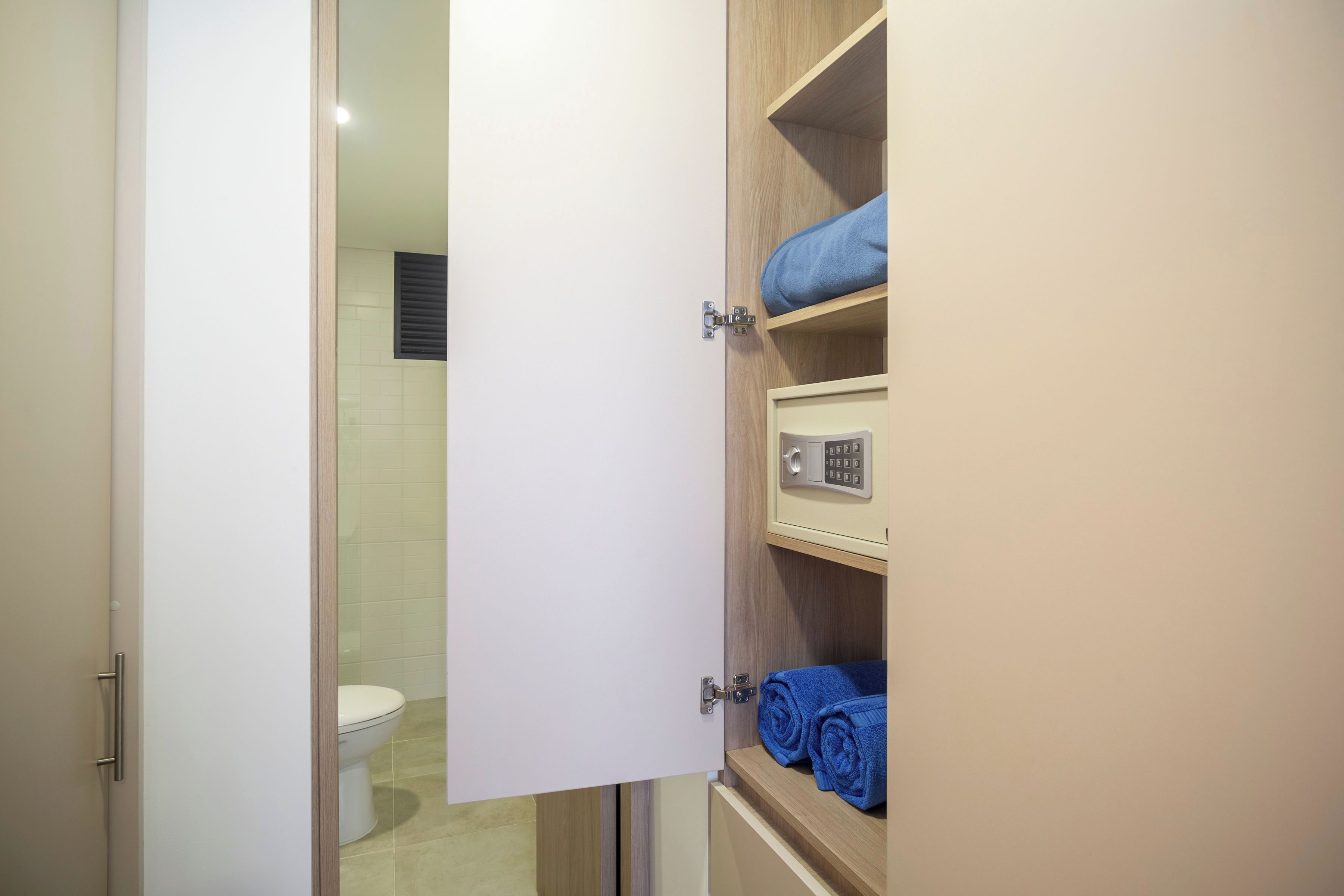 A bathroom with a toilet, a glass-enclosed shower, and a wooden cabinet with towels.