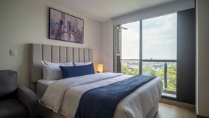 Una habitación de hotel moderna con una cama grande, cabecera, vista panorámica de la ciudad a través de un amplio ventanal y una silla.