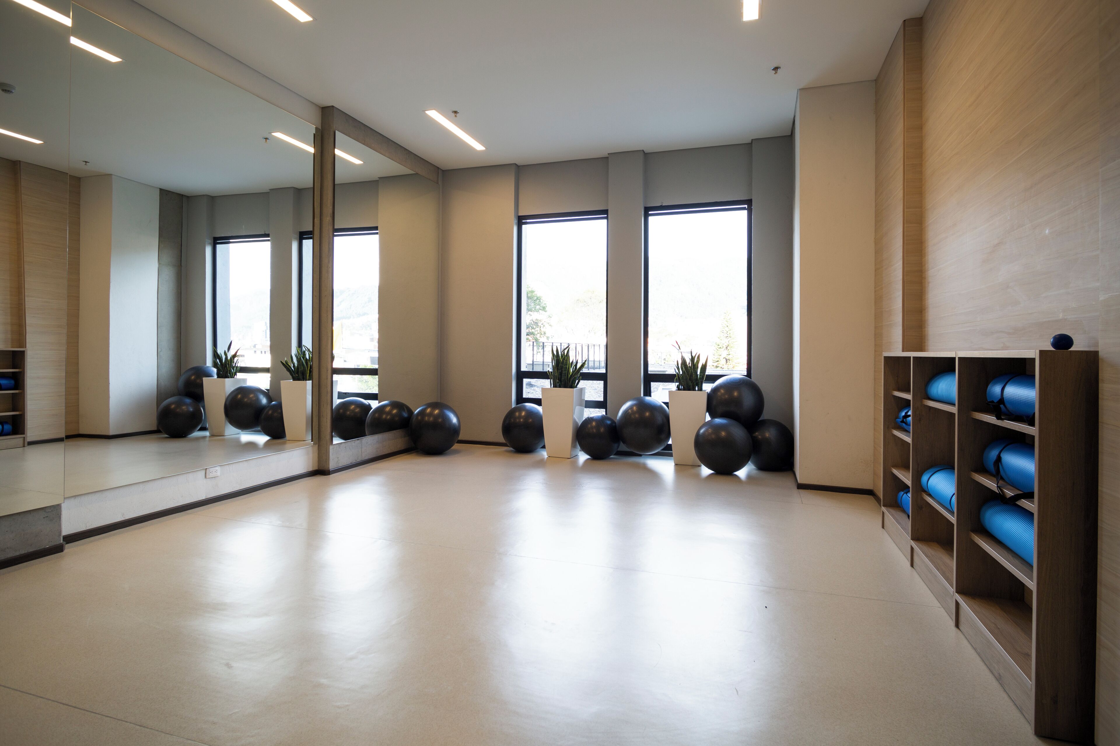 A spacious room with a large mirror, exercise balls, and shelves with blue mats.