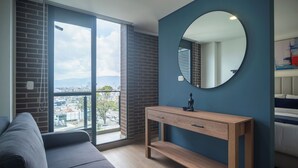 Una sala de estar moderna con un ventanal grande, un sofá, una consola de madera y un espejo redondo en la pared.