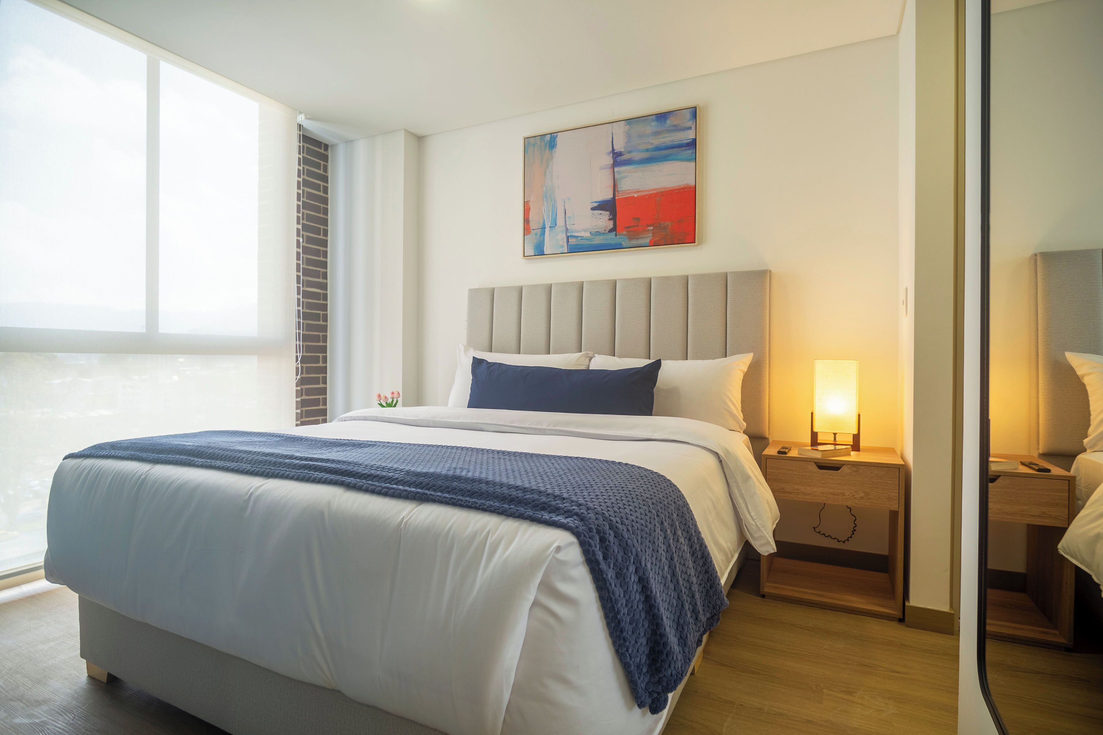 Een hotelkamer met een groot bed, nachtkastje, een lamp en een schilderij aan de muur.