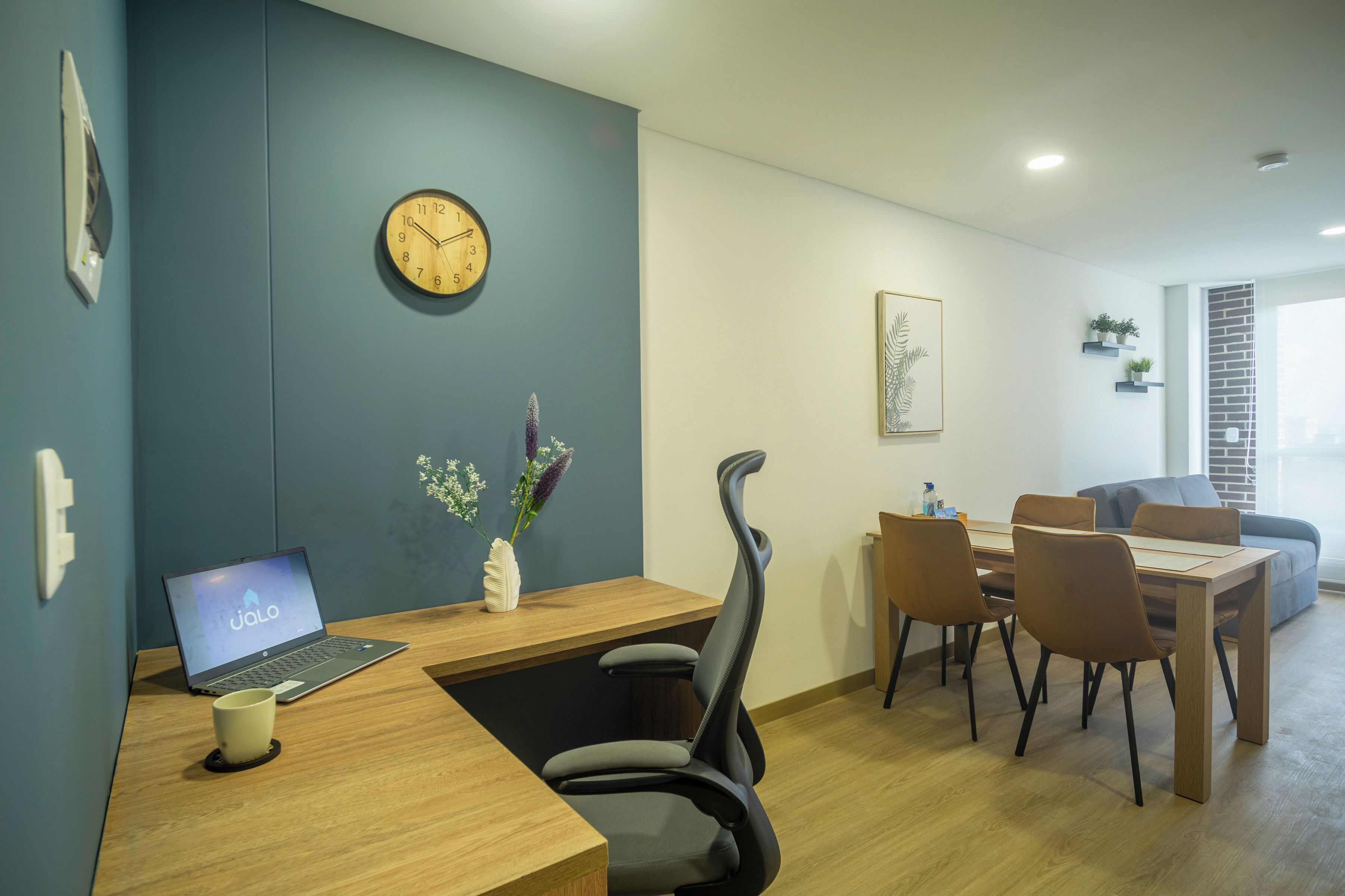A modern office space with a desk, laptop, and a clock on the wall.