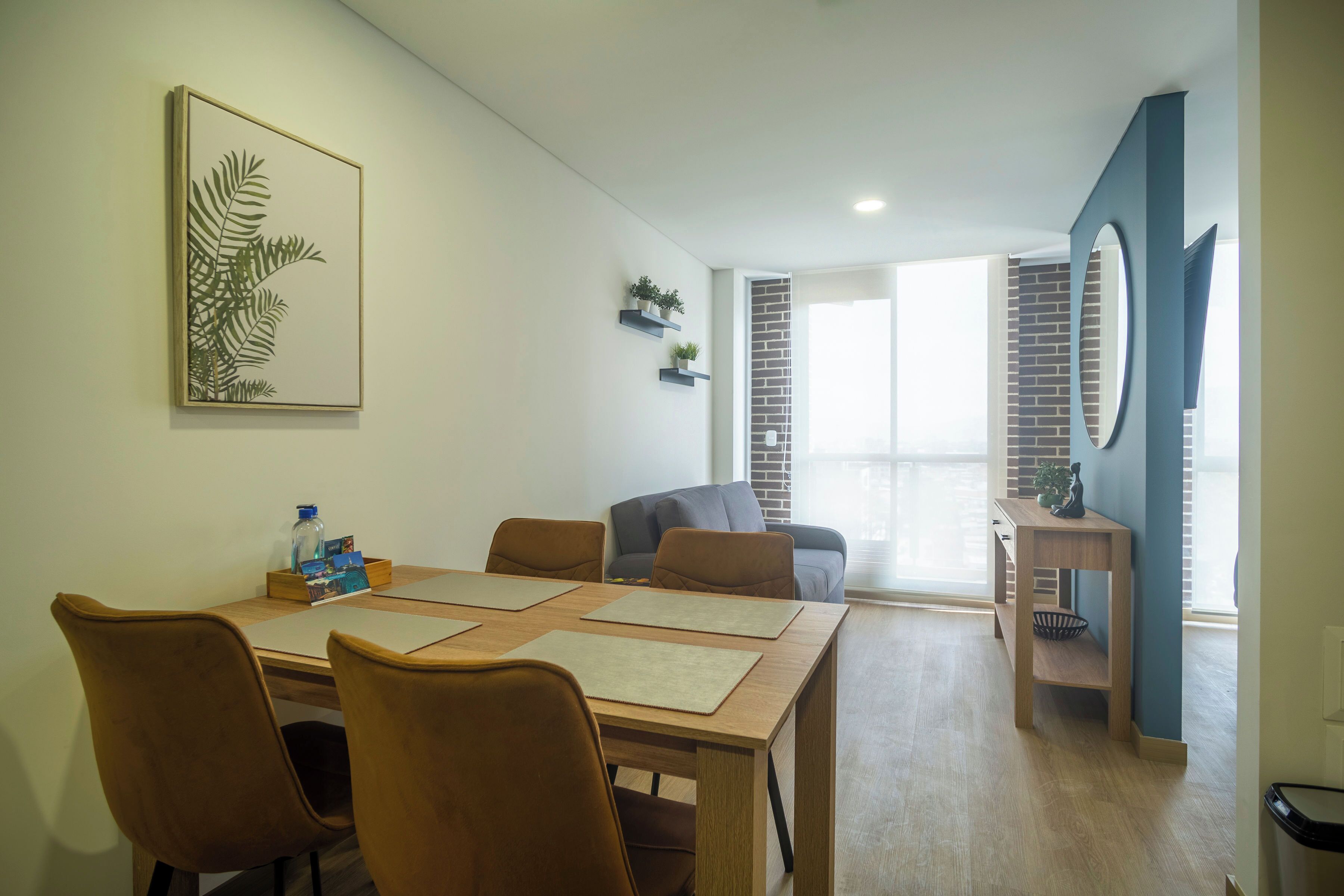 A dining area with a wooden table, four chairs, and a framed plant on the wall.