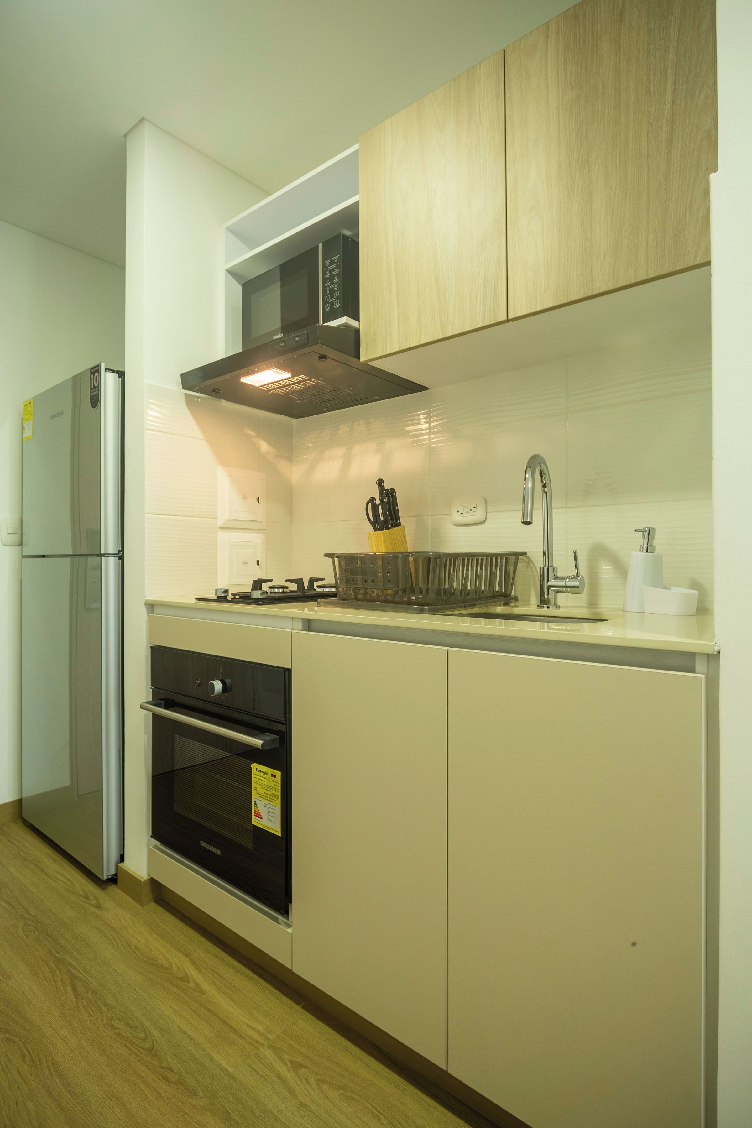 Una cocina moderna con un refrigerador de acero inoxidable, un microondas, un horno y un lavamanos con grifo.