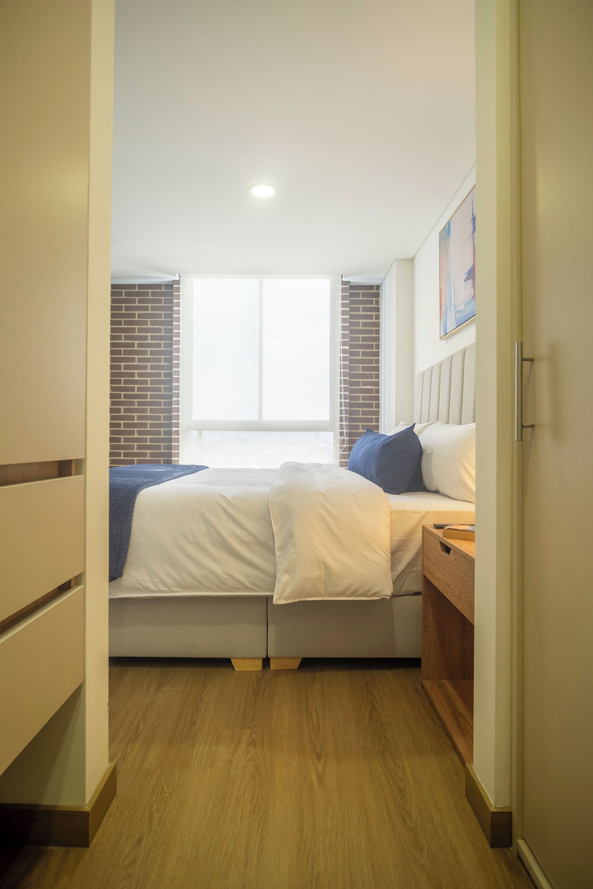 Quarto com cama, janela e parede de tijolos.