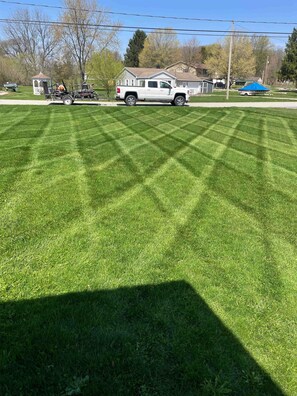 A well-maintained lawn with a lawnmower and a truck in the background.