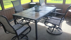 A covered patio with a table and chairs, a metal bucket, and a view of a lake and trees. - 10 passengers pontoon boat  with Golfcart INCLUDED great fishing and swimming  (Trufant)