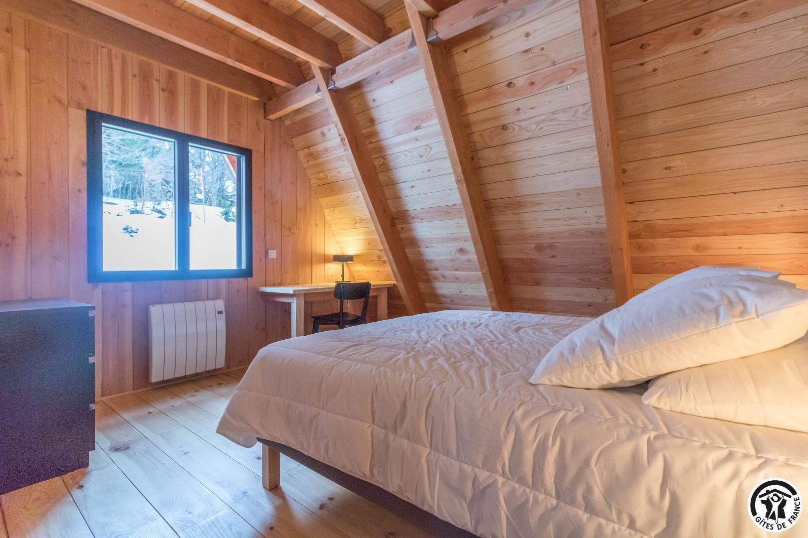 A cozy wooden room with a bed, a desk, and a window.